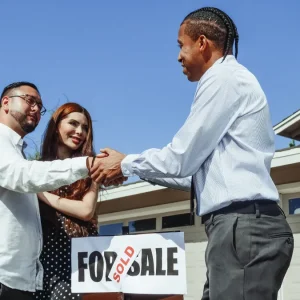 People shaking hands outside a house with a for-sale sign
