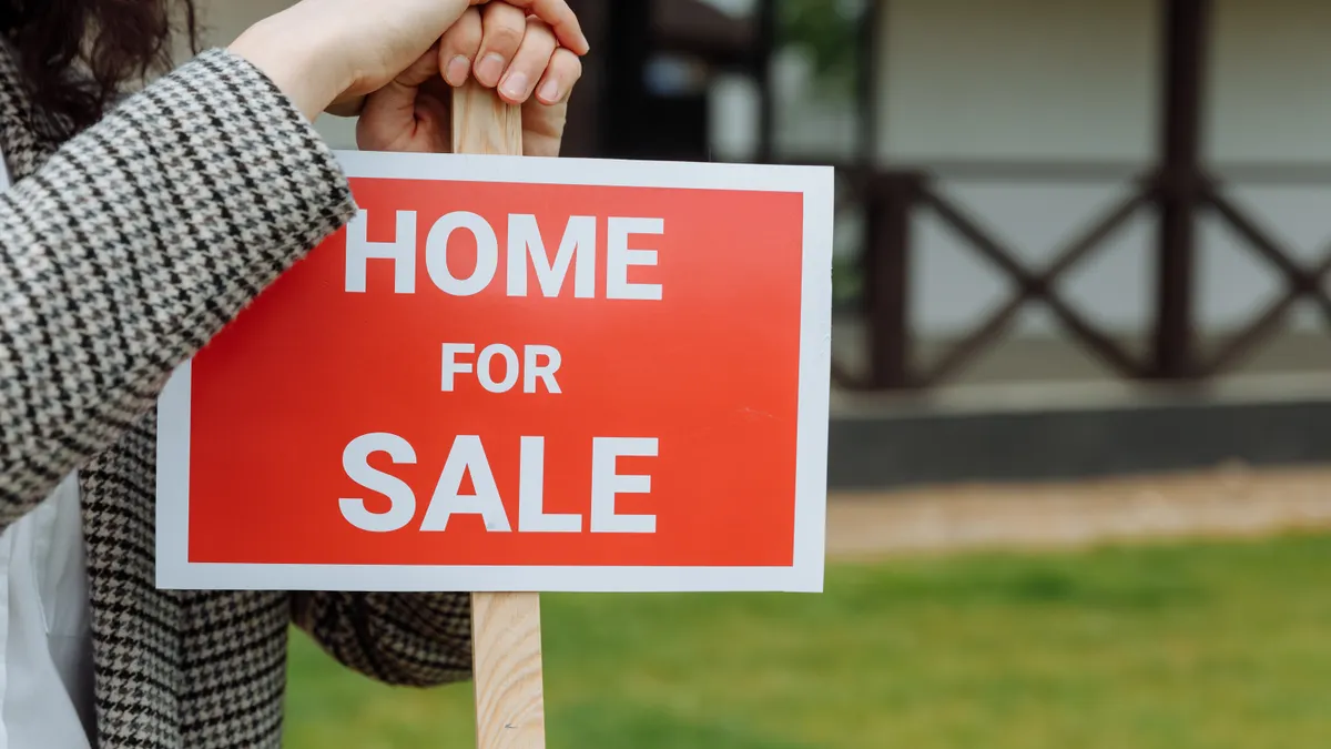 Person holding a HOME FOR SALE sign