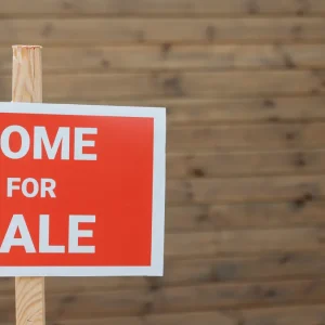 Red HOME FOR SALE sign on a wooden post