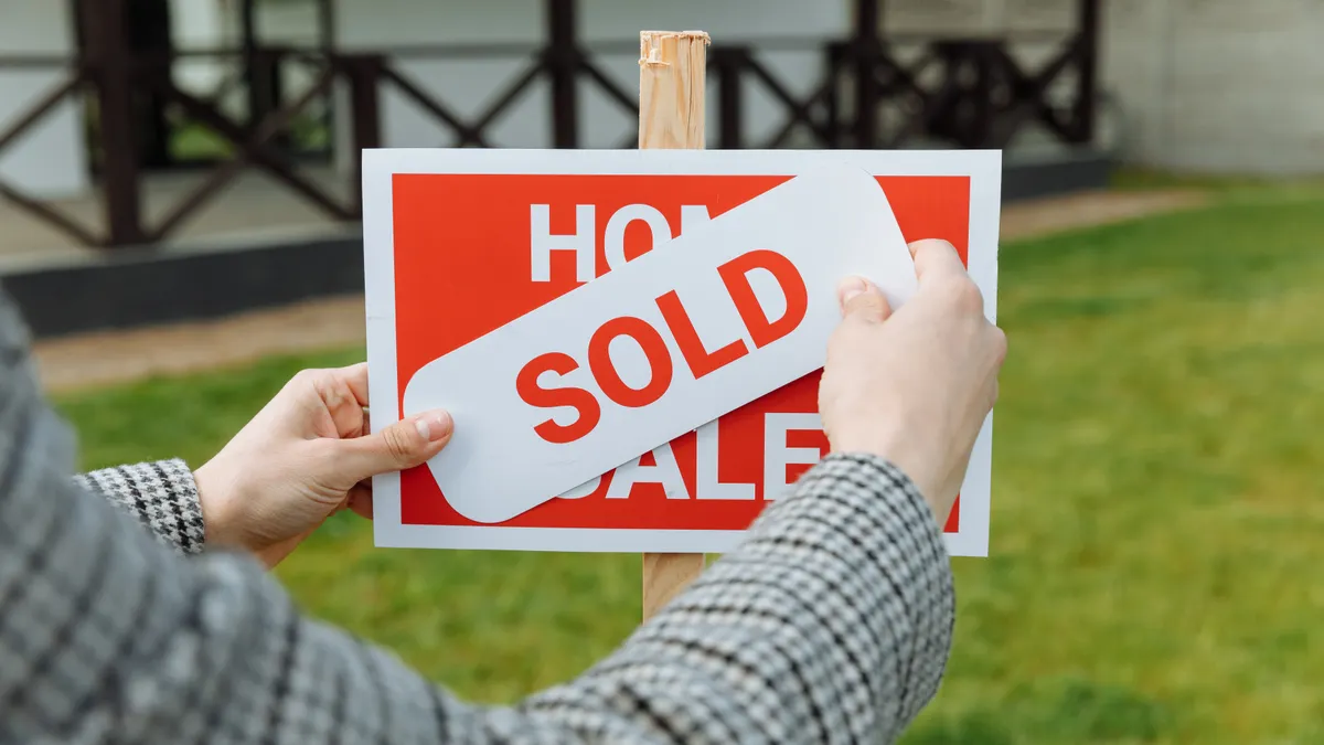 hands placing a sold sticker on a for-sale sign